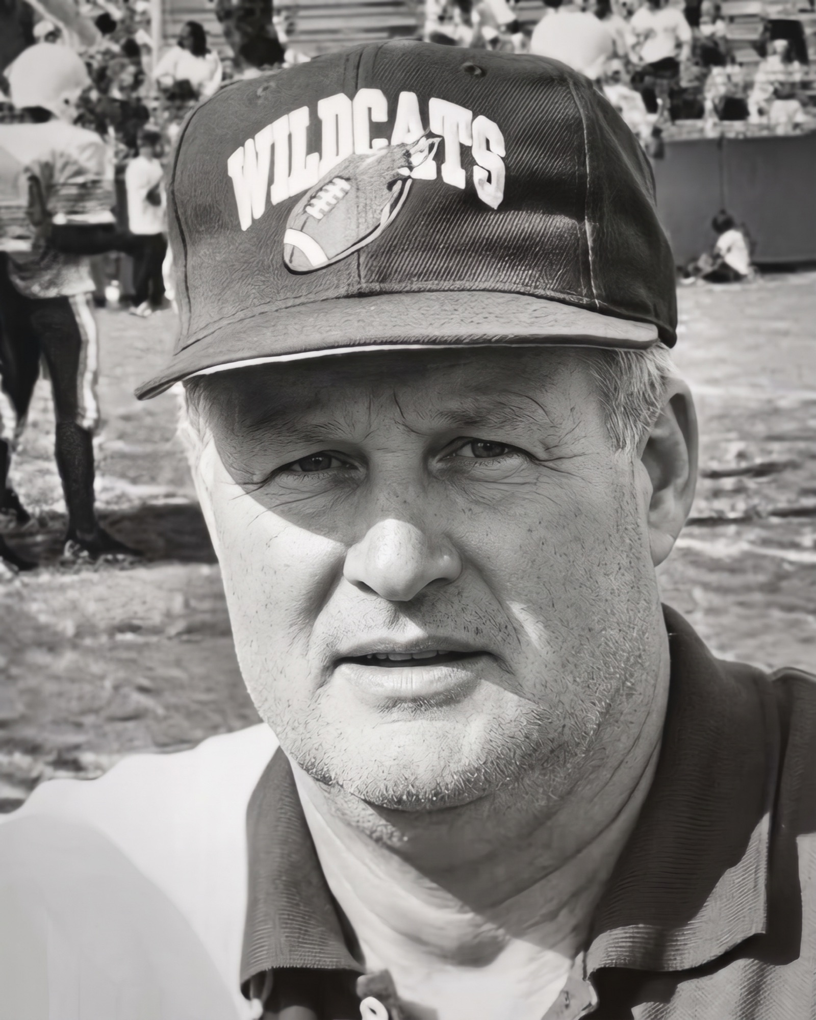 Coach Maurice Wren in a Wildcats cap at a football game, black-and-white portrait.